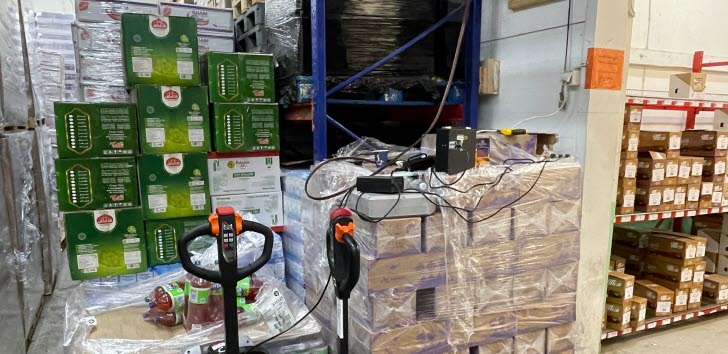 två lyfthanordningar med staplar av paketvaror i en lagerhall