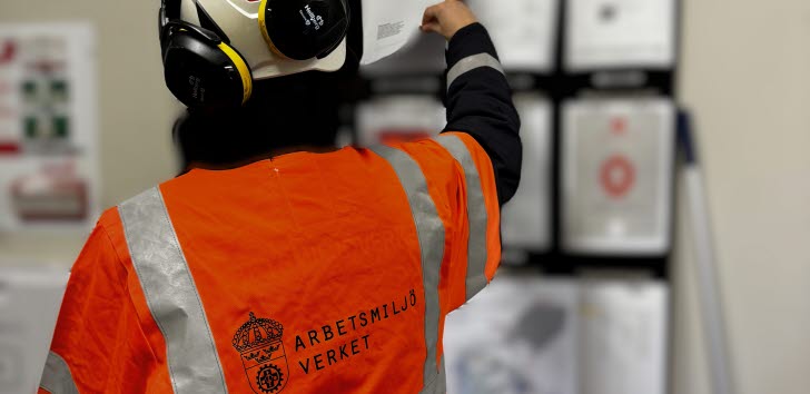 Person i röd varselklädsel bläddrar i en pärm på en anslagstavla.