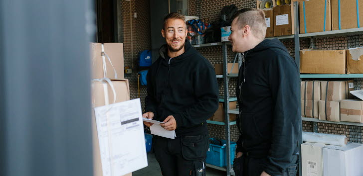 Två män står framför en hylla med kartonger