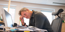Stressad man vid sitt skrivbord sneglar ned på högen med dokument