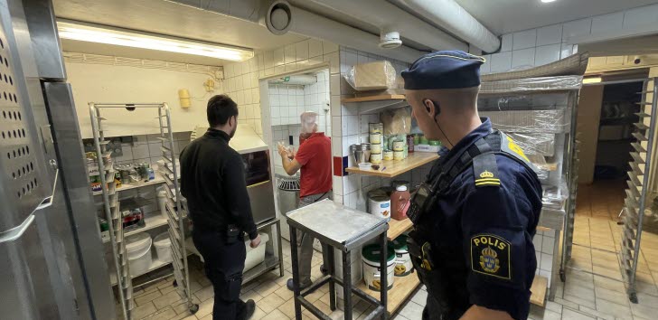 Restaurangkök med två kontrollanter varav en från polisen som står med ryggen mot kameran.