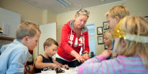 En förskolepedagog och fem barn är samlade vid ett bord och leker