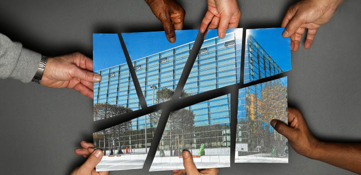 Sju händer som håller i en varsin bit som tillsammans bildar ett fotografi av en byggnad.