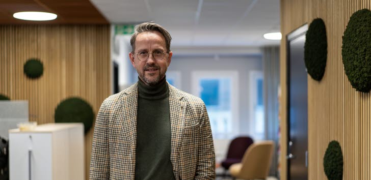 En man står i en upplyst korridor och tittar leendes in i kameran. 