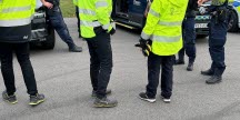 Poliser och arbetsmiljöinspektörer i gula reflexjackor vid en polisbil.