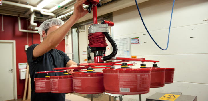 En person med hårnät använder en maskin för att lyfta flera röda burkar på en fabrik.