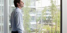 Arbetande man blickar ut genom stort fönster