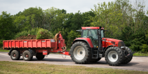Bild på röd traktor med röd vagn full med jord körandes på landsväg