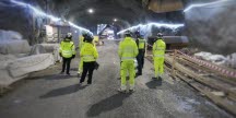 Personer i reflexkläder står i en osläckt tunnel med arbetsmaterial runt omkring.