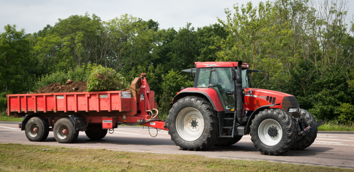 Bild på röd traktor med röd vagn full med jord körandes på landsväg