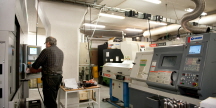 En tillverkningslokal med flera maskiner varav en maskin används av en man som trycker på maskinens knappar