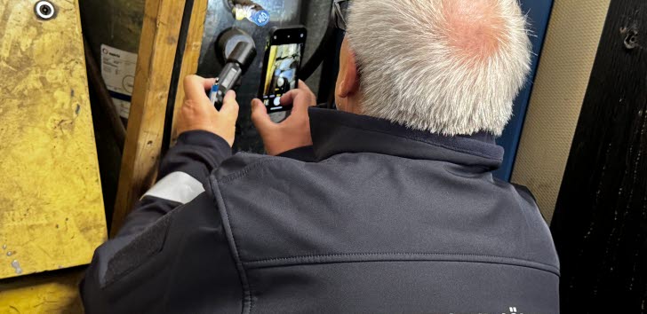En person från Arbetsmiljöverket använder en mätinstrument och en mobiltelefon vid en inspektion.
