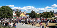 Ett gäng människor står utanför en stads ringmur i sommarsolen. 