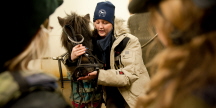 En kvinna står bredvid en häst i stallgången, bild, fotograf: Mia Åkerström