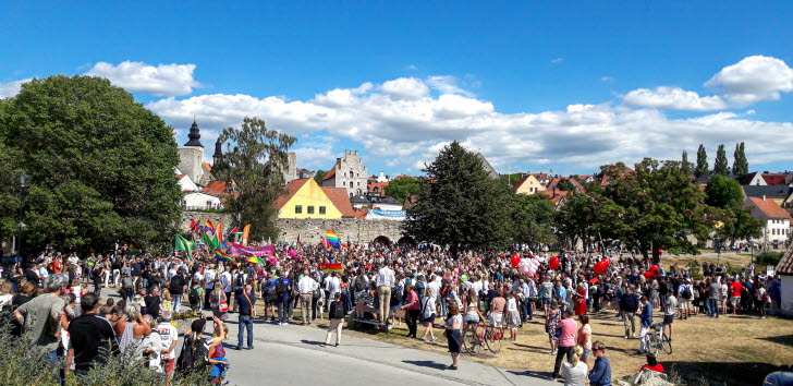 Ett gäng människor står utanför en stads ringmur i sommarsolen.