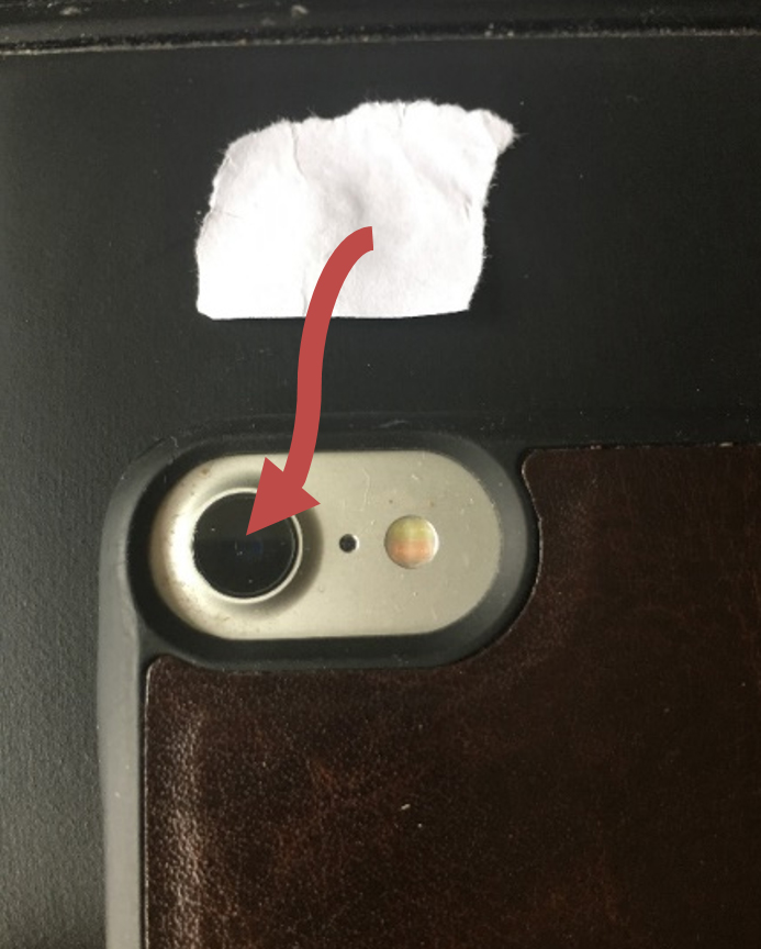 Bild som visar delar av bakstycket på en iPhone och en liten papperslapp med en röd pil som, pekar förklarande att den ska placeras över kamerans lins.