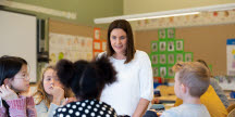 En kvinna som står i ett klassrum framför en grupp barn.