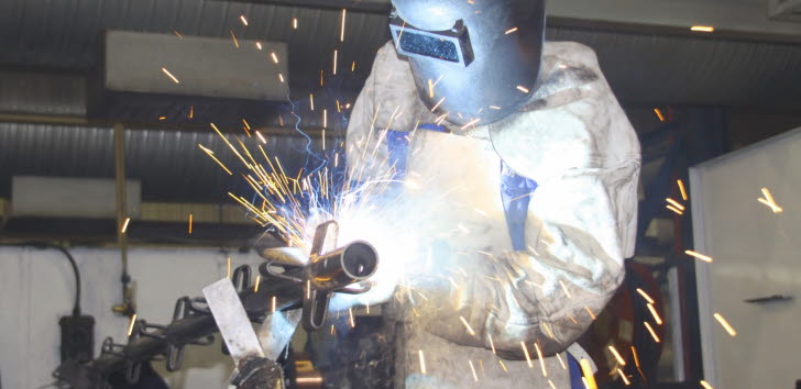 En svetsare står och svetsar i full skyddsutrustning med gnistor omkring sig.