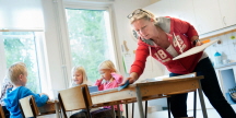 Kvinna bredvid barn torkar ett bord på en förskola