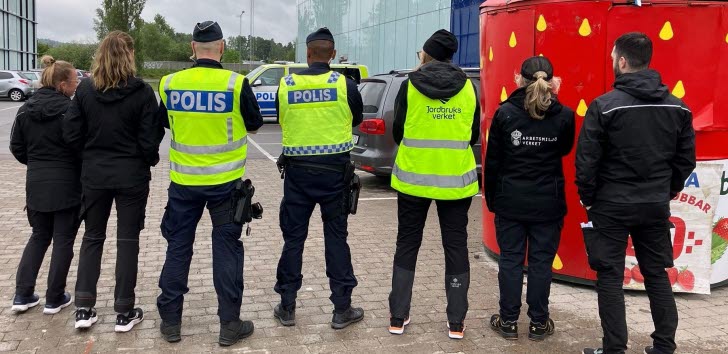 Sju personer står med ryggarna mot kameran, flera har västar med text "polis", "arbetsmiljöverket", "jordbruksverket".