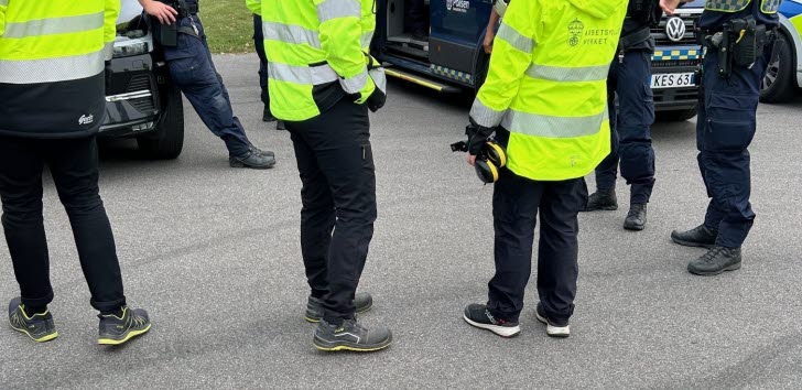 Poliser och arbetsmiljöinspektörer i gula reflexjackor vid en polisbil.