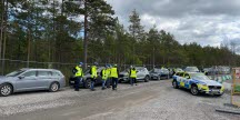 En grupp inspektörer och kontrollanter från flera olika myndigheter står på en parkeringsplats med polisbil i förgrunden.
