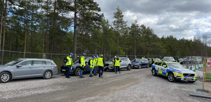 En grupp inspektörer och kontrollanter från flera olika myndigheter står på en parkeringsplats med polisbil i förgrunden.
