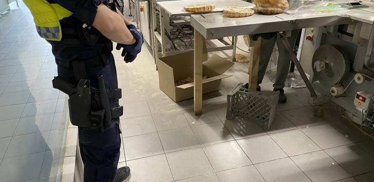 En polisman står framför en brödmaskin där en arbetstagare står och arbetar.