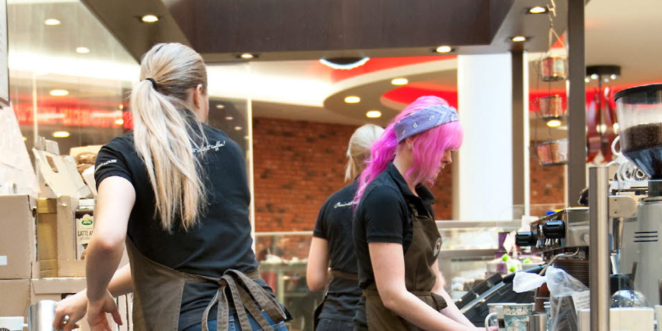 Bild på tre unga kvinnor som jobbar bakom bardisken på ett kafé