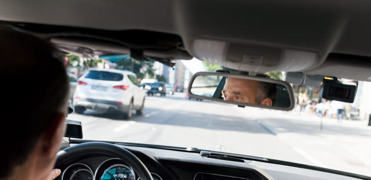 Bild tagen från baksätet på en taxi. Vi ser föraren i backspegeln.