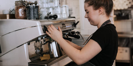 Ung kvinna använder en espressomaskin på ett kafé.