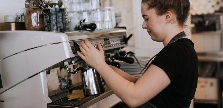 Ung kvinna använder en espressomaskin på ett kafé.