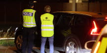 Två personer står framför en bil med ryggen vänd mot kameran. Personerna har gula västar med texten "polisen" och "kronofogden".