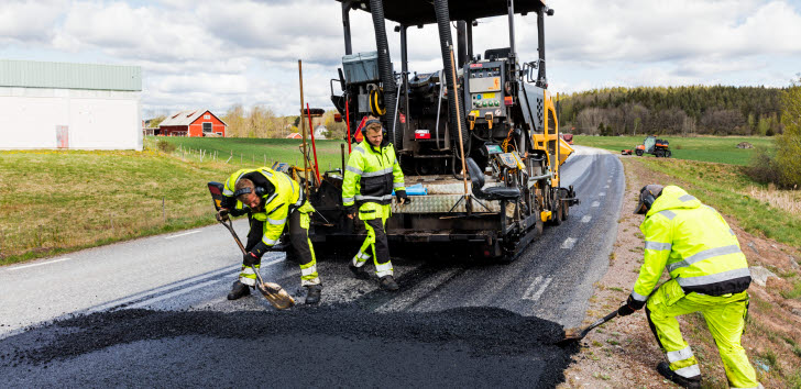 Tre asfaltsläggare arbetar med att lägga asfalt på en landsväg.