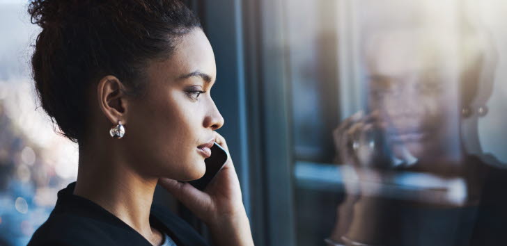 Kvinna i profil pratar i mobiltelefon och tittar ut genom ett fönster.
