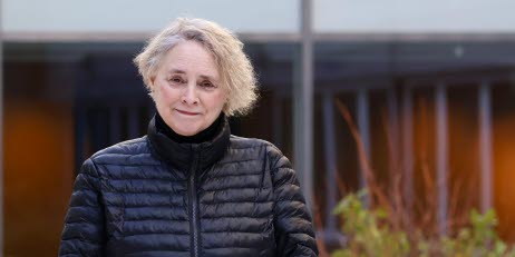 Person i svart jacka, står framför en byggnad.