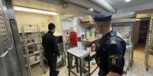 Restaurangkök med två kontrollanter varav en från polisen som står med ryggen mot kameran.