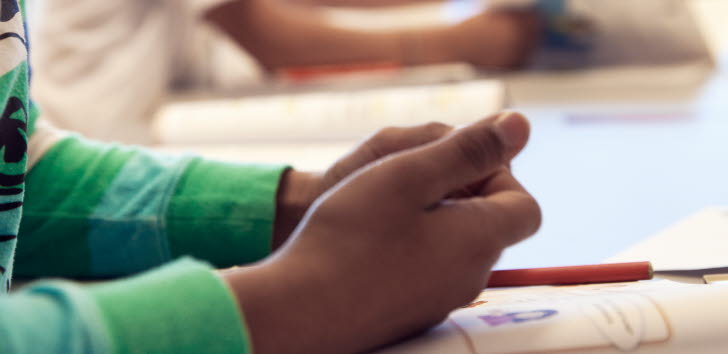 Bild på en skolelevs händer ovanför en skolbok.