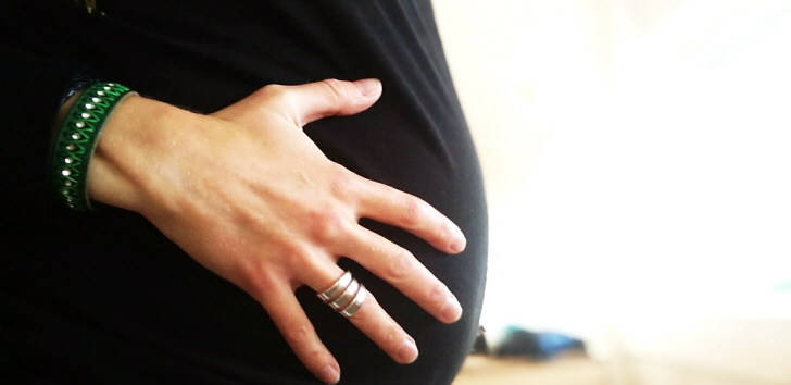 Närbild på en gravid mage. Kvinnan håller sin hand på magen.