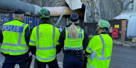 Fyra personer i reflexvästar från polisen och Arbetsmiljöverket utför en inspektion utanför en tunnel på en byggarbetsplats.