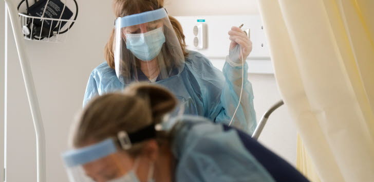 Två kvinnor med munskydd och visir i en sjukhusmiljö