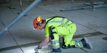Bild på byggjobbare med arbetskläder, knäskydd, hjälm och pannlampa som flytspacklar skarvarna i ett betonggolv