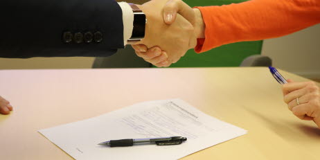Bild på två händer som skakar hand över ett kontrakt.