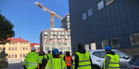 En grupp myndighetskontrollater syns bakifrån under en kontrollinsats på en byggarbetsplats.