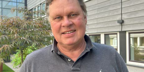 Projektledare Magnus Henriksson, klädd i grå pikétröja, står utomhus framför en modern byggnad.