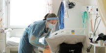 Bild från en geriatrisk avdelning på ett sjukhus. En kvinnlig sköterska i full skyddsmundering pysslar om en patient.