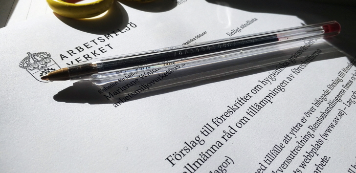 Bild på sax, penna, häftapparat liggandes på ett dokument