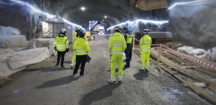 Personer i reflexkläder står i en osläckt tunnel med arbetsmaterial runt omkring.
