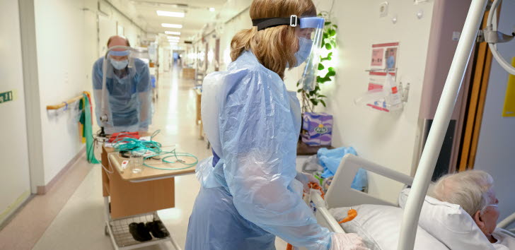 Vårdpersonal med munskydd och visir som rör sig i en sjukhuskorridor