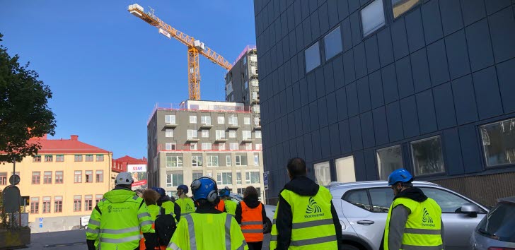 Ryggar på en grupp arbetsplatskontrollanter från olika myndigheter som inspekterar en byggarbetsplats.
